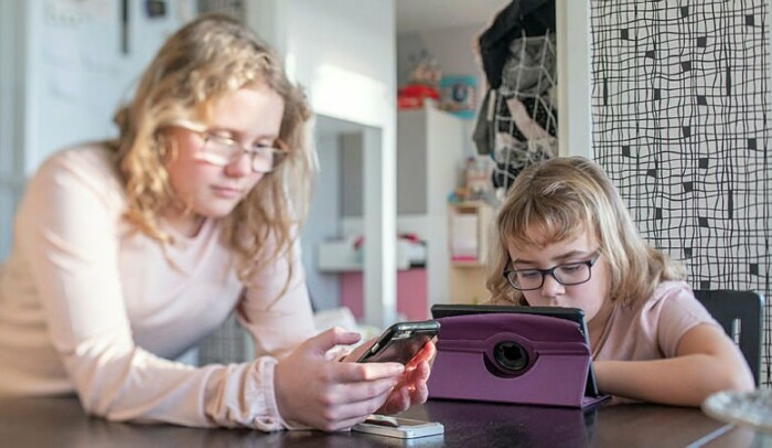 Två flickor sitter vid ett matbord med varsin skärm.